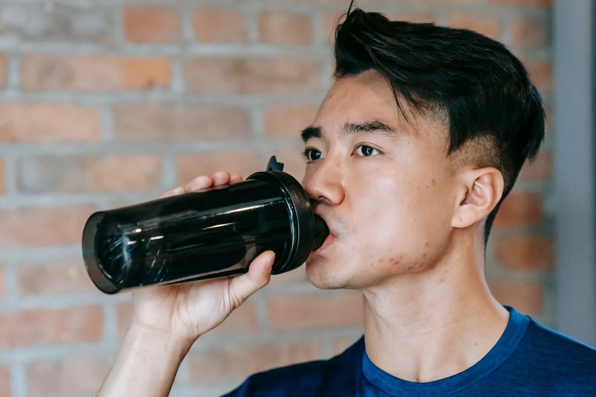 Un uomo in abbigliamento sportivo beve da uno shaker nero durante una pausa dall’allenamento