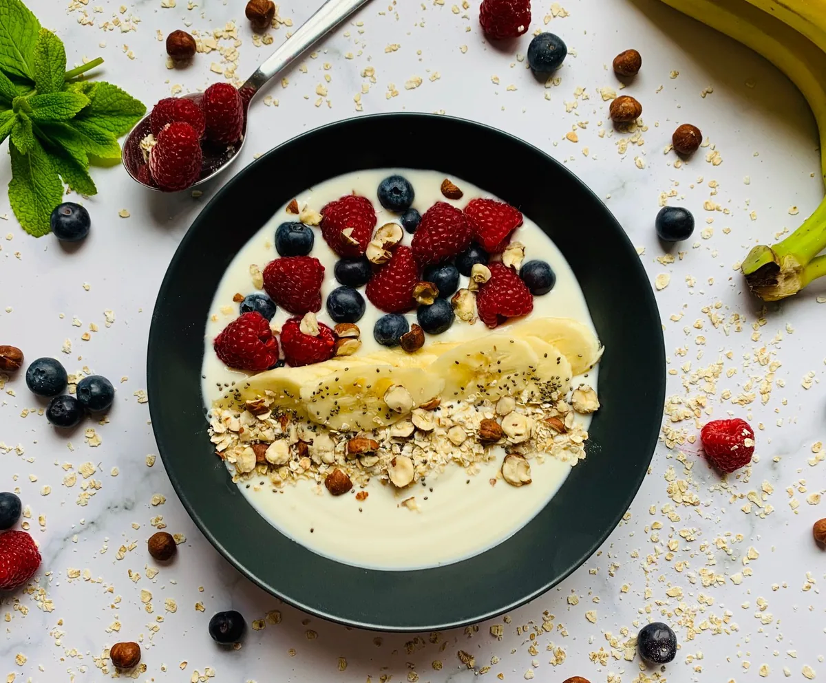 Ciotola con yogurt, fiocchi di avena, banana, frutti di bosco e nocciole