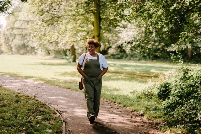 Una donna cammina sorridendo lungo un sentiero alberato nel parco